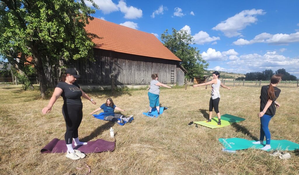 Reiterinnen bei Fitnessübungen auf Matten im Freien vor dem Stall